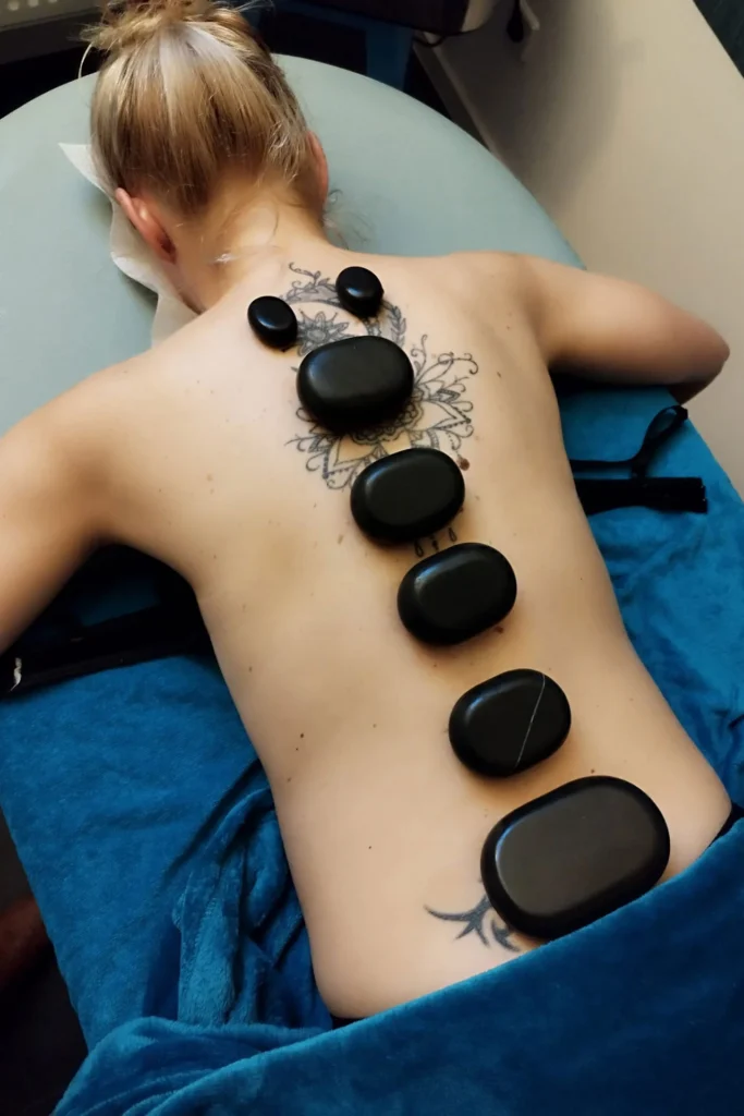 Physiotherapie Mandy Dannehl in Dessau Roßlau - Bereit für den Wandel – der erste Schritt zur Heilung. Gutschein - Therapieangebote - Privatleistungen- Hot-Stone-Massage - Frau mit freiem Oberkörper liegt auf dem Bauch - auf dem Rücken die heissen Steine